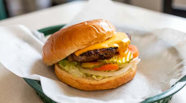 Cheeseburger with melted yellow cheese, beef patty, lettuce, onions, tomatoes, and pickles on a bun.