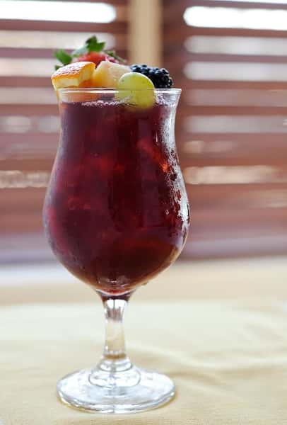 Sangria in tall glass with grapes, berries, and orange in it