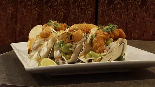 three fish tacos with fried fish with guacamole and lime