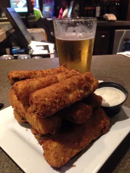 stack of mozzerella sticks with a side of white sauce and a cup of beer