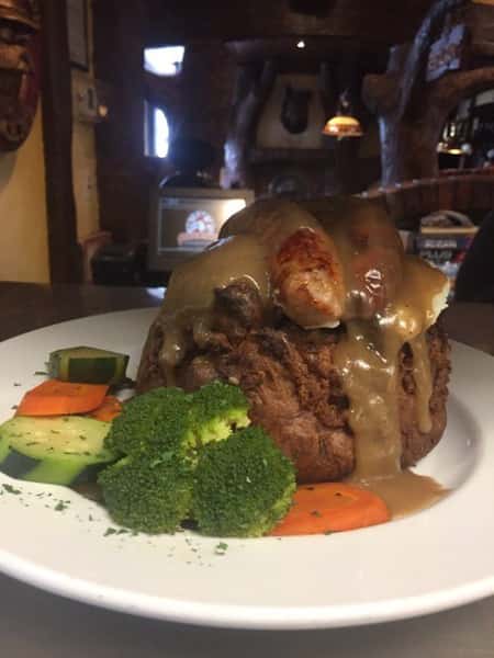 large meatball with sausage and gravy on top. a side of cucumbers, carrots and broccoli