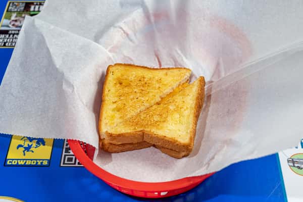 Golden-brown grilled cheese sandwich cut diagonally and served in a red plastic basket lined with parchment paper, set atop a blue Louisiana-themed table.