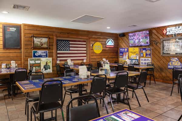Cozy dining area at Darrell's restaurant with wood-paneled walls, patriotic decor including an American flag, blue laminated tables, and sports-themed beer ads creating a laid-back, family-friendly vibe