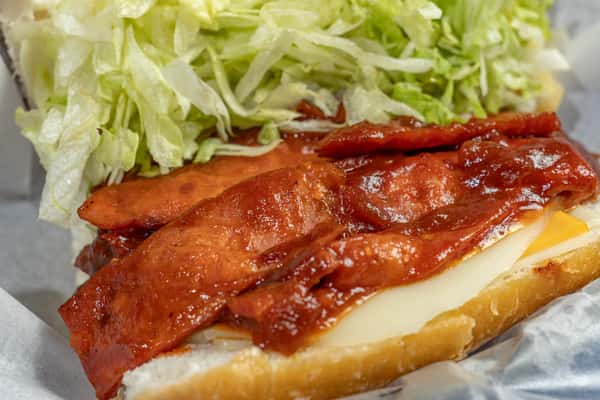 Close-up of a po'boy sandwich layered with crispy bacon glazed in smoky barbecue sauce, melted cheese, and shredded lettuce on a soft, toasted hoagie roll.