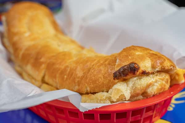 Golden-brown stuffed bread roll with a flaky, buttery crust, slightly curled at the edges and served in a red plastic basket lined with parchment paper—perfect as a savory side or appetizer.