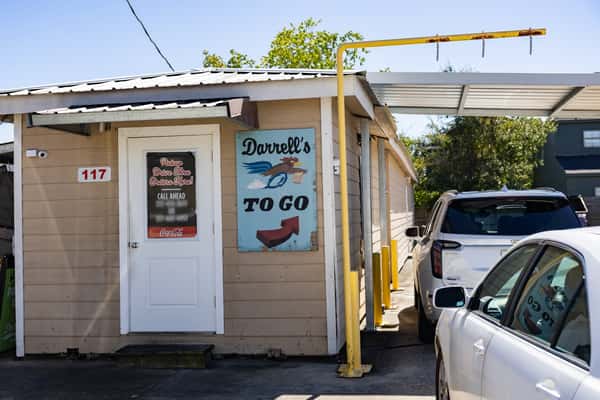 Drive-thru pickup building for Darrell's To Go, featuring a vintage-style painted sign and vehicles in line under a metal awning on a sunny day.