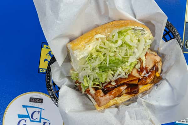 Turkey and barbecue po'boy sandwich in a paper-lined basket, filled with sliced deli turkey, tangy barbecue sauce, shredded lettuce, and melted cheese on a fresh Louisiana-style roll.