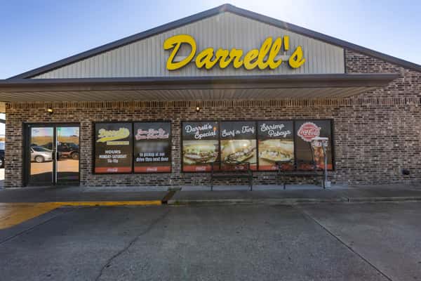 Frontal view of Darrell's po'boy shop showcasing its large yellow logo and window graphics promoting signature sandwiches like the Surf n' Turf and Shrimp Po'boy.