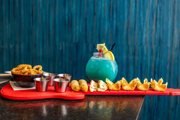 Assorted Asian appetizers including fried calamari, spring rolls, dumplings, and wontons, served with sauces and a blue cocktail.