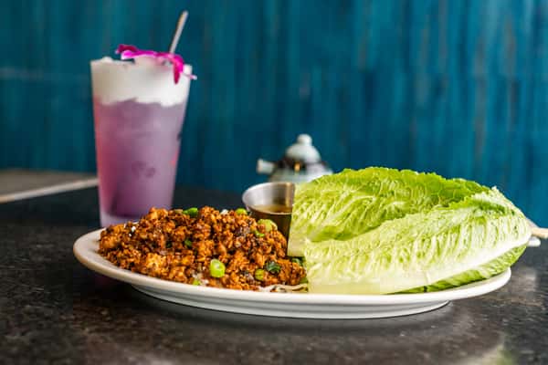 Spiced ground chicken lettuce wraps with dipping sauce, served with a purple coconut drink topped with a vibrant orchid flower.