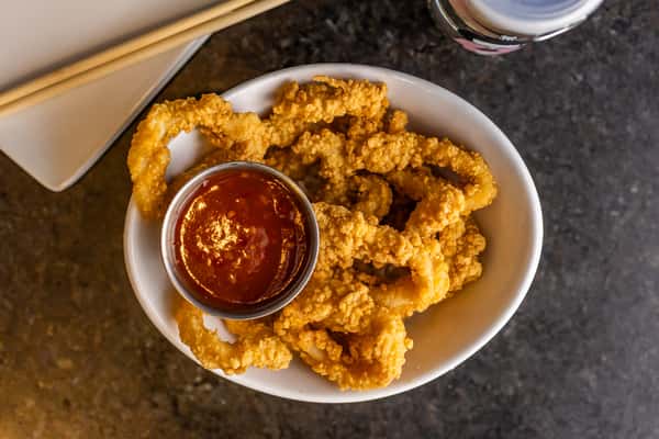 Crispy golden calamari rings served in a white bowl with a side of tangy red dipping sauce.