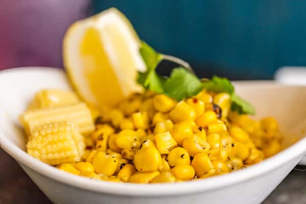 Seasoned grilled corn kernels with baby corn, garnished with cilantro and a wedge of lemon.