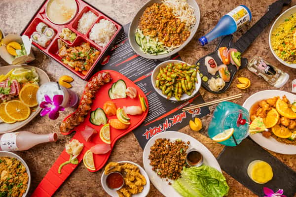 Colorful spread of Asian fusion dishes including sushi, lettuce wraps, bento box, edamame, fried rice, and vibrant cocktails.