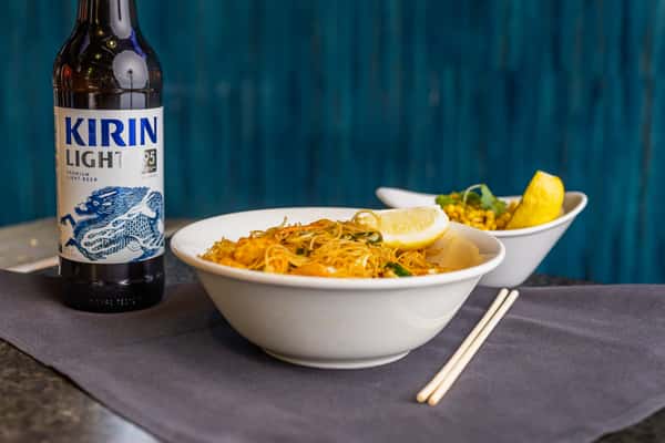 Stir-fried vermicelli noodles with lemon wedge, served with a side of fried rice and Kirin Light beer.