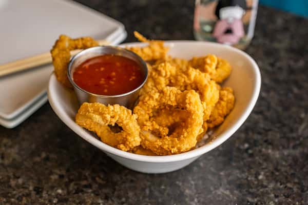 Crispy fried calamari rings served in a white bowl with sweet chili dipping sauce on the side.