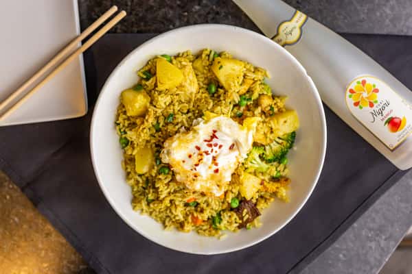Pineapple fried rice with vegetables topped with a fried egg and chili flakes, served alongside a chilled mango Nigori sake.