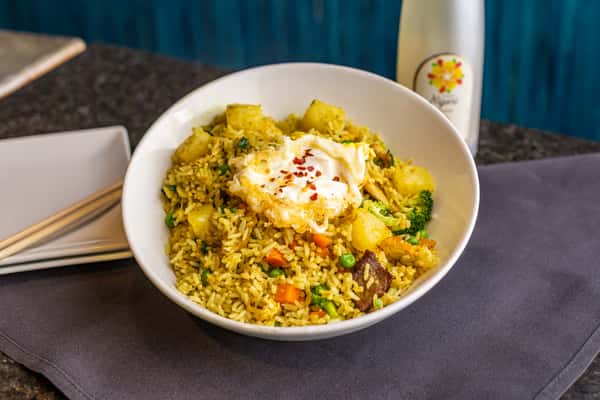 Pineapple fried rice with vegetables topped with a fried egg and chili flakes, served alongside a chilled mango Nigori sake.