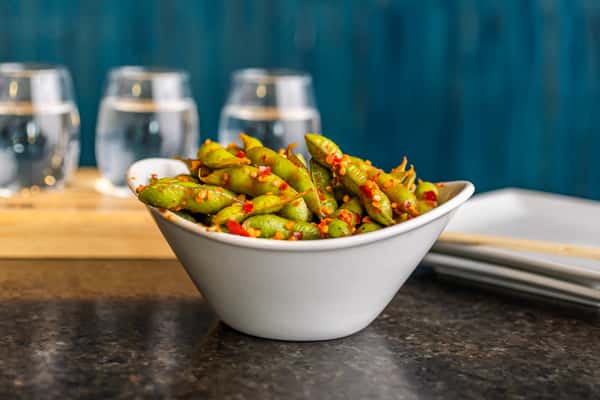 Spicy garlic edamame tossed in chili flakes, served in a modern white bowl on a dark tabletop.