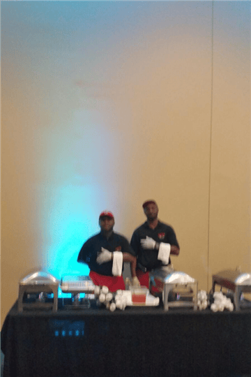 two chefs standing behind a catering style table with metal trays