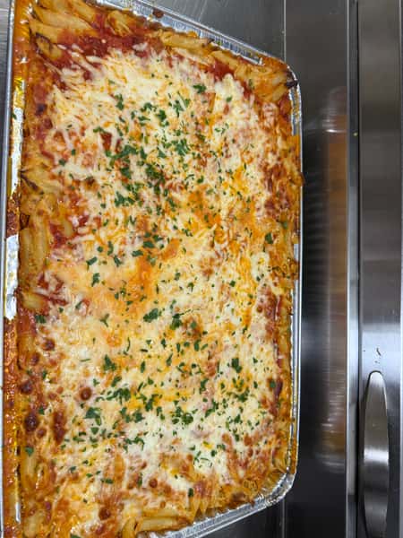 Overhead view of cheesy baked ziti pasta in a foil tray, layered with marinara sauce, melted mozzarella, and garnished with fresh chopped herbs—ideal for Italian catering or buffet service.