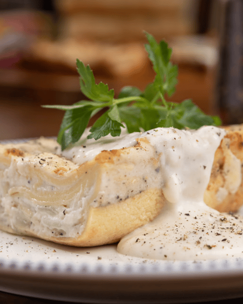 Close-up of a creamy white lasagna slice layered with pasta, ricotta, and Alfredo sauce, garnished with fresh parsley and cracked black pepper.