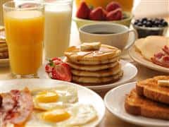 Short Stack of pancakes, two sunny side up eggs, glasses of milk and orange juice, cup of coffe, strawberries in a bowl.