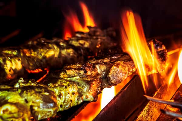 Whole fish roasting over an open flame, showcasing fire-grilled seafood preparation in a restaurant kitchen.