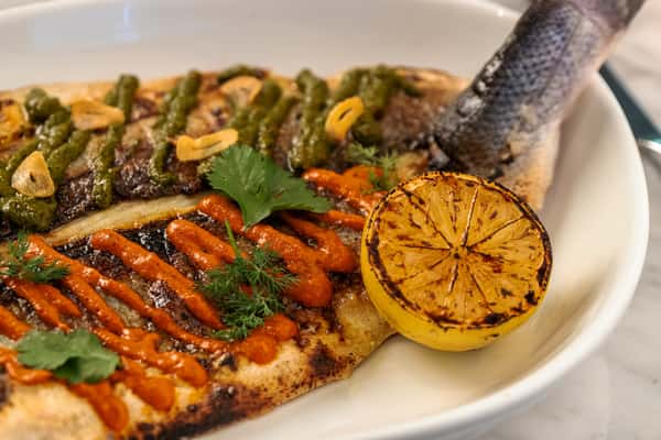 Grilled whole fish with charred lemon, roasted vegetables, and fresh herbs in a Mediterranean-style presentation.