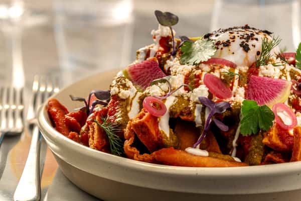 Colorful Mediterranean salad topped with cheese, fresh vegetables, herbs, and edible flower garnish.