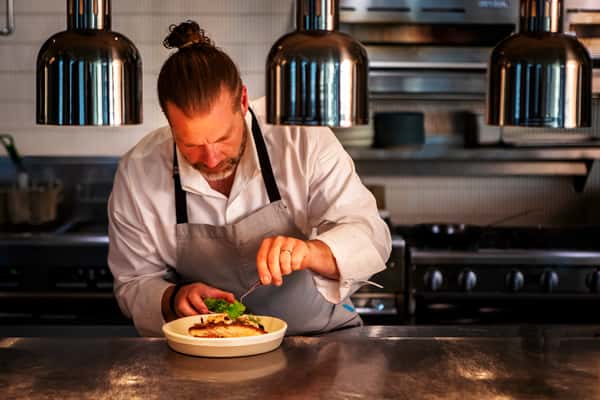 Chef carefully plating a gourmet dish with precision in a modern restaurant kitchen.