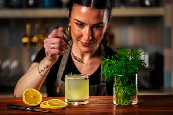 Bartender carefully garnishing a fresh cocktail with herbs and citrus in a stylish restaurant bar.