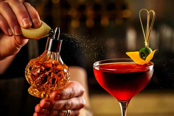 Bartender misting a handcrafted red cocktail with citrus garnish for an elevated cocktail experience.