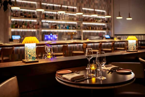 Elegant restaurant dining table with candlelight, wine glasses, and warm ambient lighting overlooking a sophisticated cocktail bar.