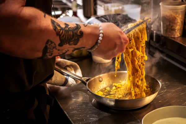 Chef hand-pulling fresh pasta from a cheese wheel, creating a rich and indulgent pasta dish.
