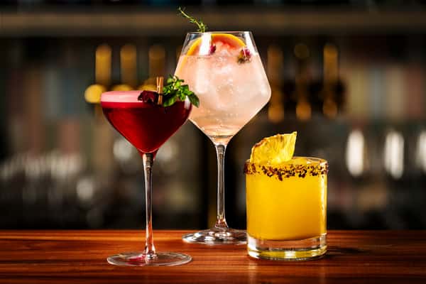 Craft cocktails featuring a berry martini, citrus spritz, and tropical pineapple drink on a polished bar top.