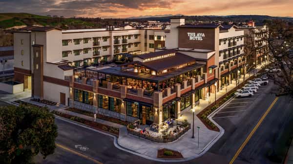 Aerial view of a contemporary restaurant and rooftop bar illuminated at sunset in a vibrant mixed-use district.