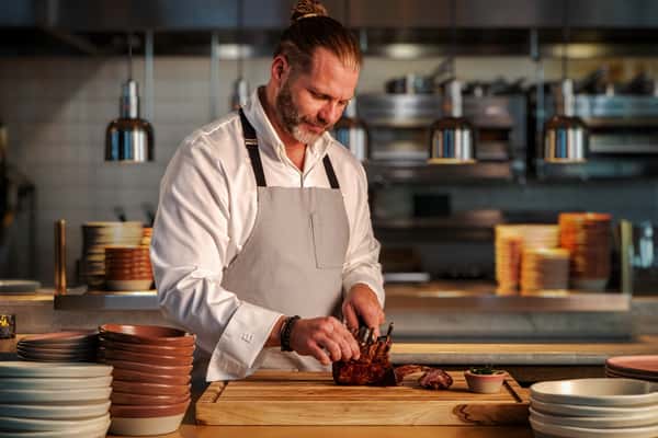 Chef expertly carving and plating premium roasted meat in an open kitchen with warm restaurant lighting.