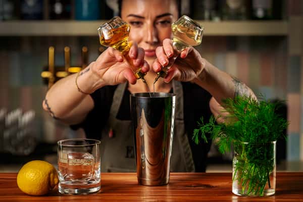 Bartender garnishing a craft cocktail with fresh olives over a polished metal shaker in an upscale bar.