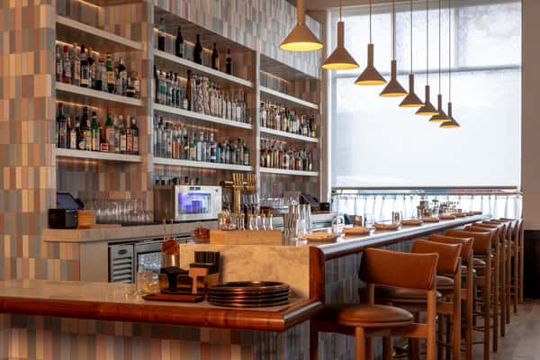 Modern restaurant bar with premium spirits, marble countertops, leather bar seating, and warm pendant lighting in an upscale dining space.