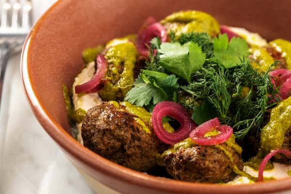 Crispy falafel topped with fresh herbs, pickled onions, and Mediterranean vegetables in a rustic bowl.