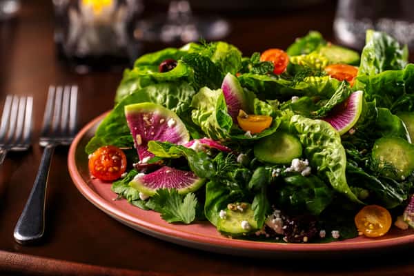 Fresh mixed greens salad with cherry tomatoes, herbs, and vibrant seasonal vegetables in an elegant presentation.