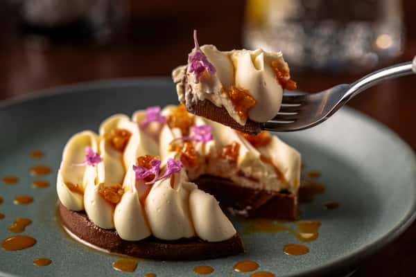 Elegant plated dessert topped with edible flowers, caramel drizzle, and a forkful of creamy pastry.