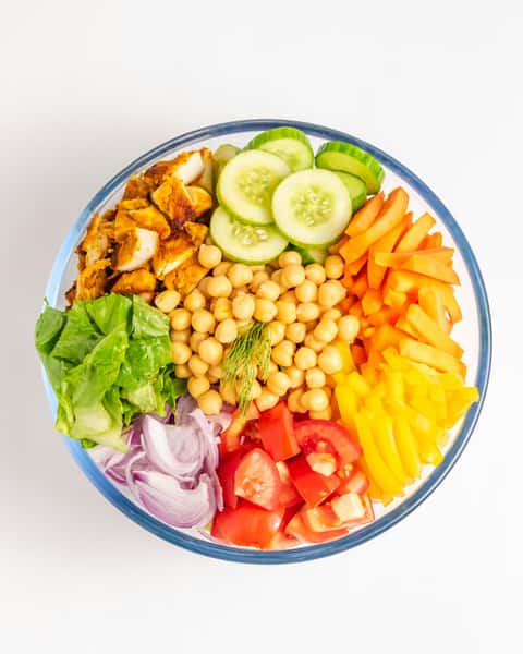 Colorful salad bowl with chickpeas, grilled chicken, cucumber, bell peppers, tomato, red onion, and lettuce