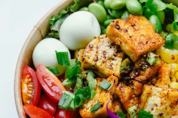 Spicy tofu bowl with cherry tomatoes, boiled eggs, green onions, corn, and edamame