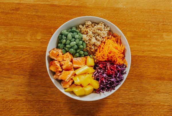 Healthy bowl with salmon, quinoa, edamame, shredded carrots, red cabbage, and mango
