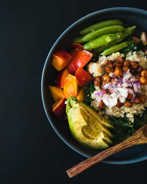 Colorful quinoa bowl with avocado, chickpeas, red onion, snap peas, and fresh fruit
