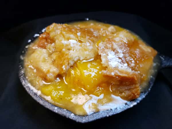 Golden brown peach cobbler dusted with powdered sugar, served in a mini black skillet from Southern Blues.