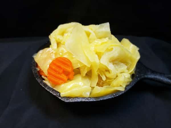 Bright yellow braised cabbage and carrot slices served in a mini black cast iron skillet.