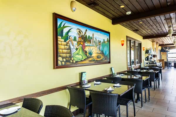 Inviting outdoor patio dining area with black tables, chairs, colorful Mexican artwork, and a warm, casual atmosphere.