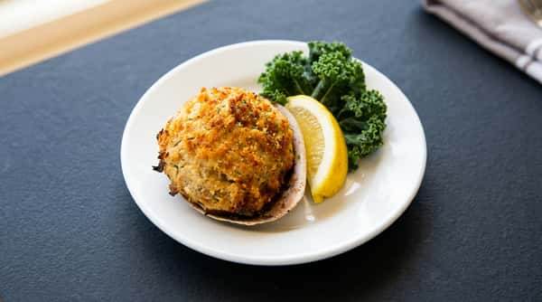 A perfectly seared crab cake is plated with a lemon wedge and fresh greens, offering a crisp exterior and a flavorful, seafood-rich center.